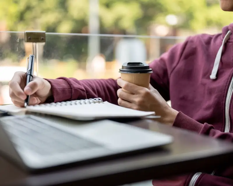 A young man is journalling and drinking a coffee. He has a life he wants to make better through coaching and self-awareness.